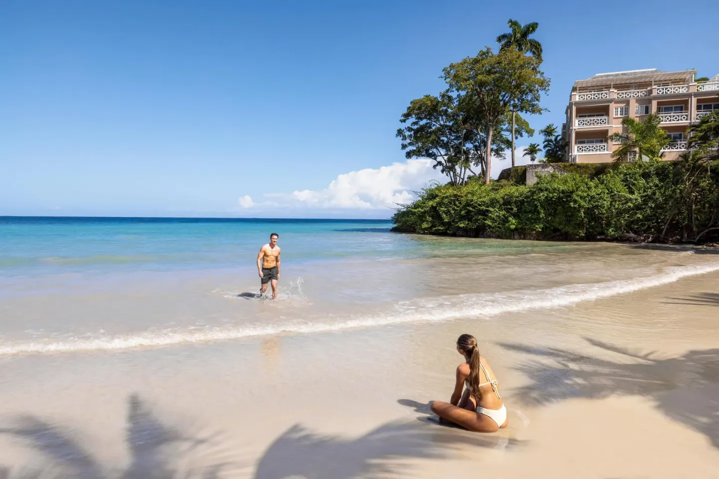 Couple relaxing on a sandy beach beside calm blue water at Couples Sans Souci.