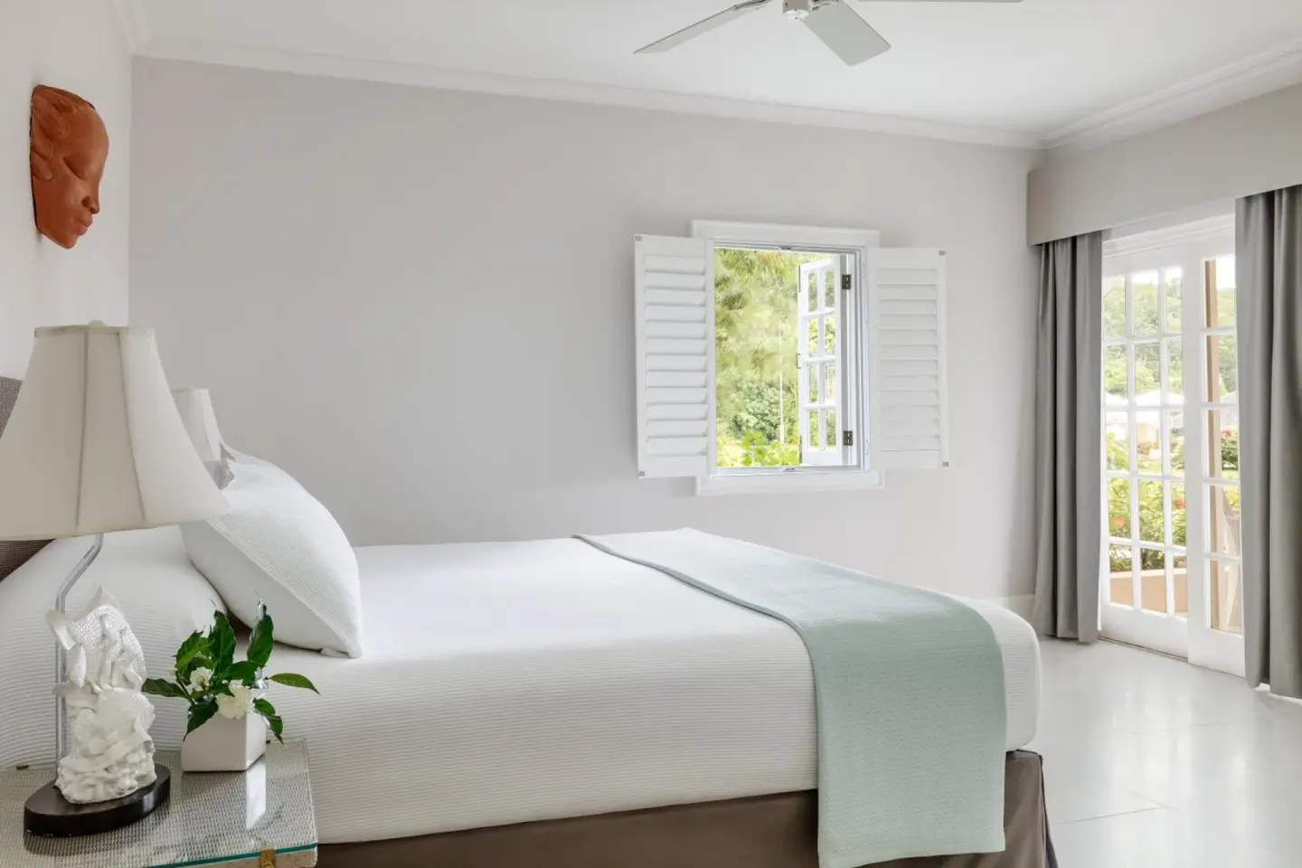 Bright guest room with a white bed and garden-facing windows at Couples Sans Souci.