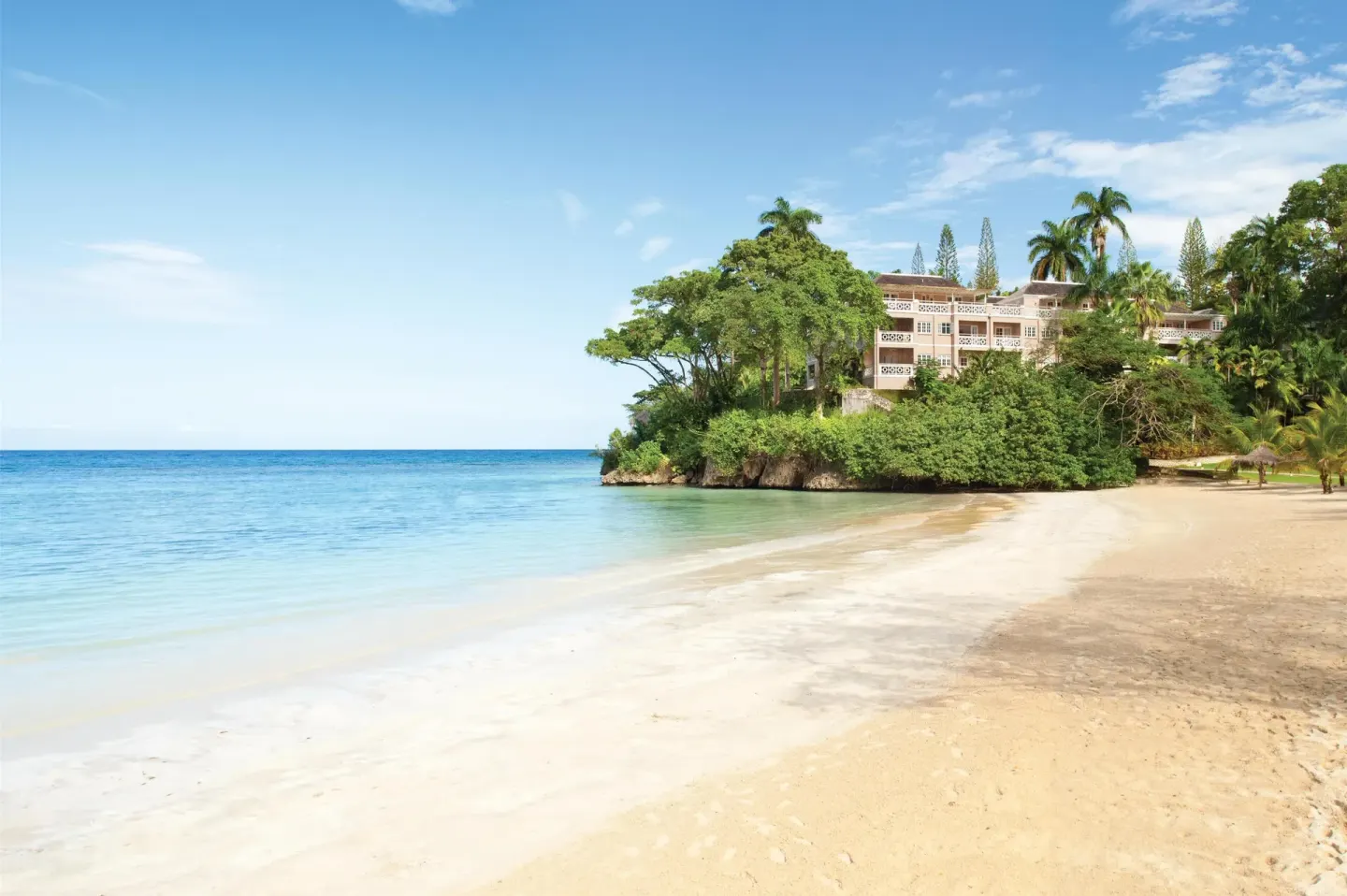 Quiet sandy beach with turquoise water and hillside buildings at Couples Sans Souci.