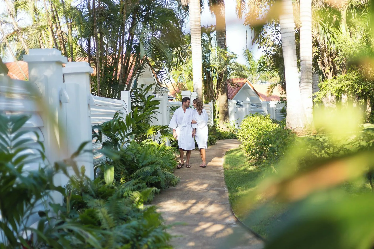 Couple in robes walking along a palm-lined garden path at Couples Tower Isle.