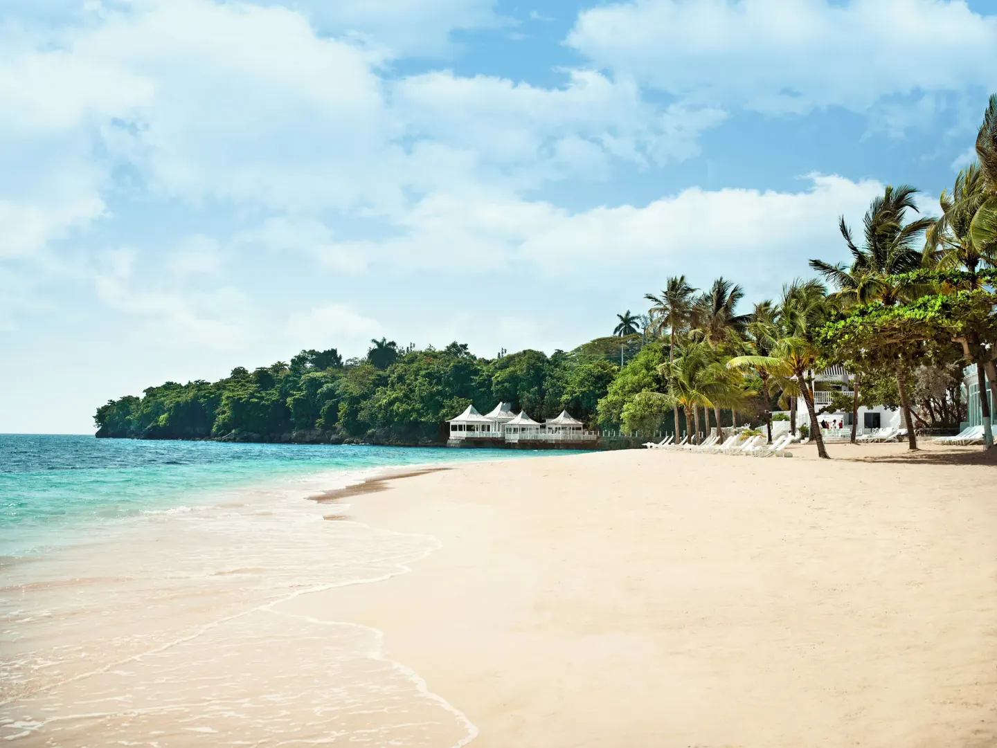 Sandy beach with turquoise water, palms, and loungers at Couples Tower Isle.