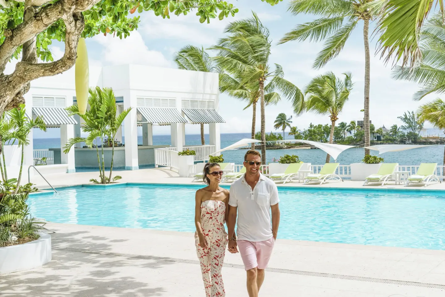 Couple walking beside a pool with palms and ocean beyond at Couples Tower Isle.