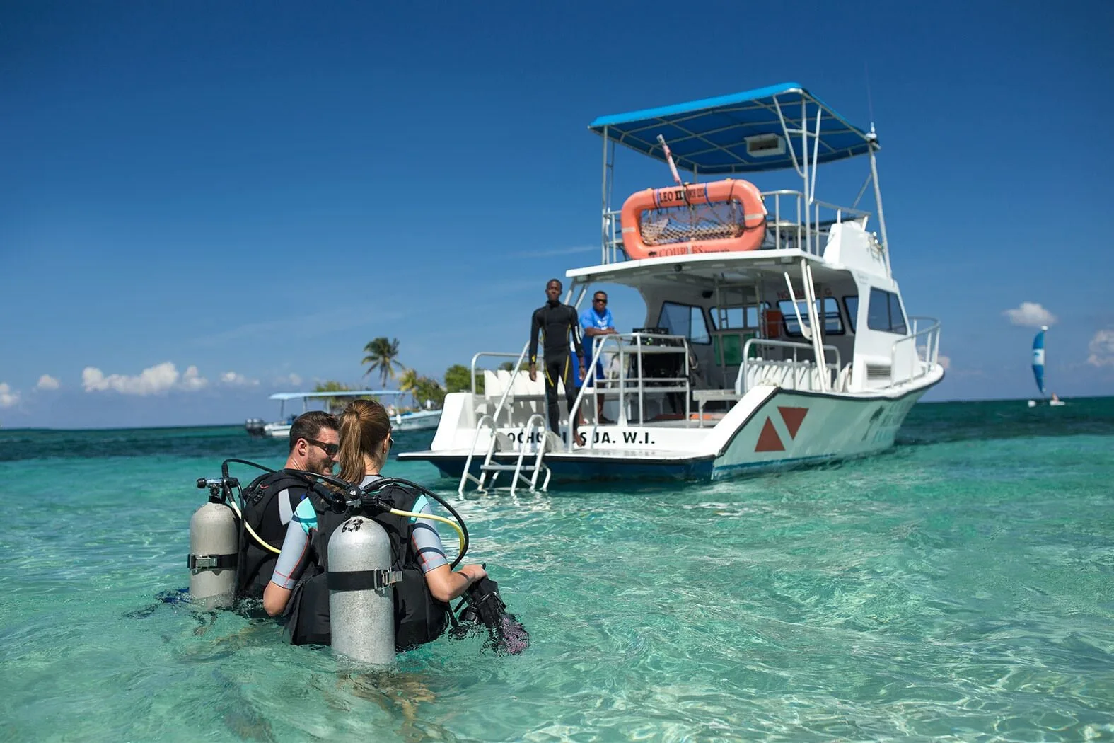 Scuba divers stand in clear water beside a dive boat at Couples Tower Isle.