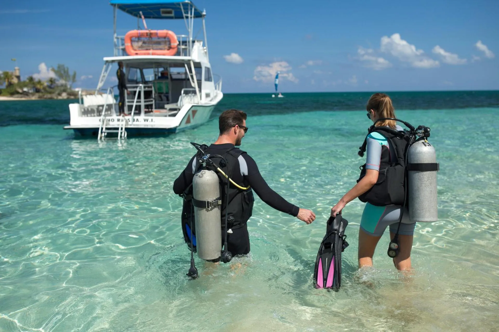 Scuba divers walk through clear water toward a dive boat at Couples Tower Isle.