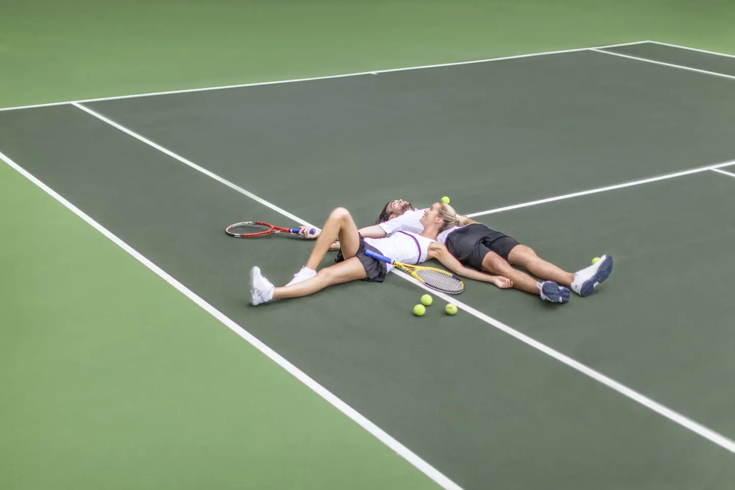 Two guests rest with tennis rackets and balls on a court at Couples Tower Isle.