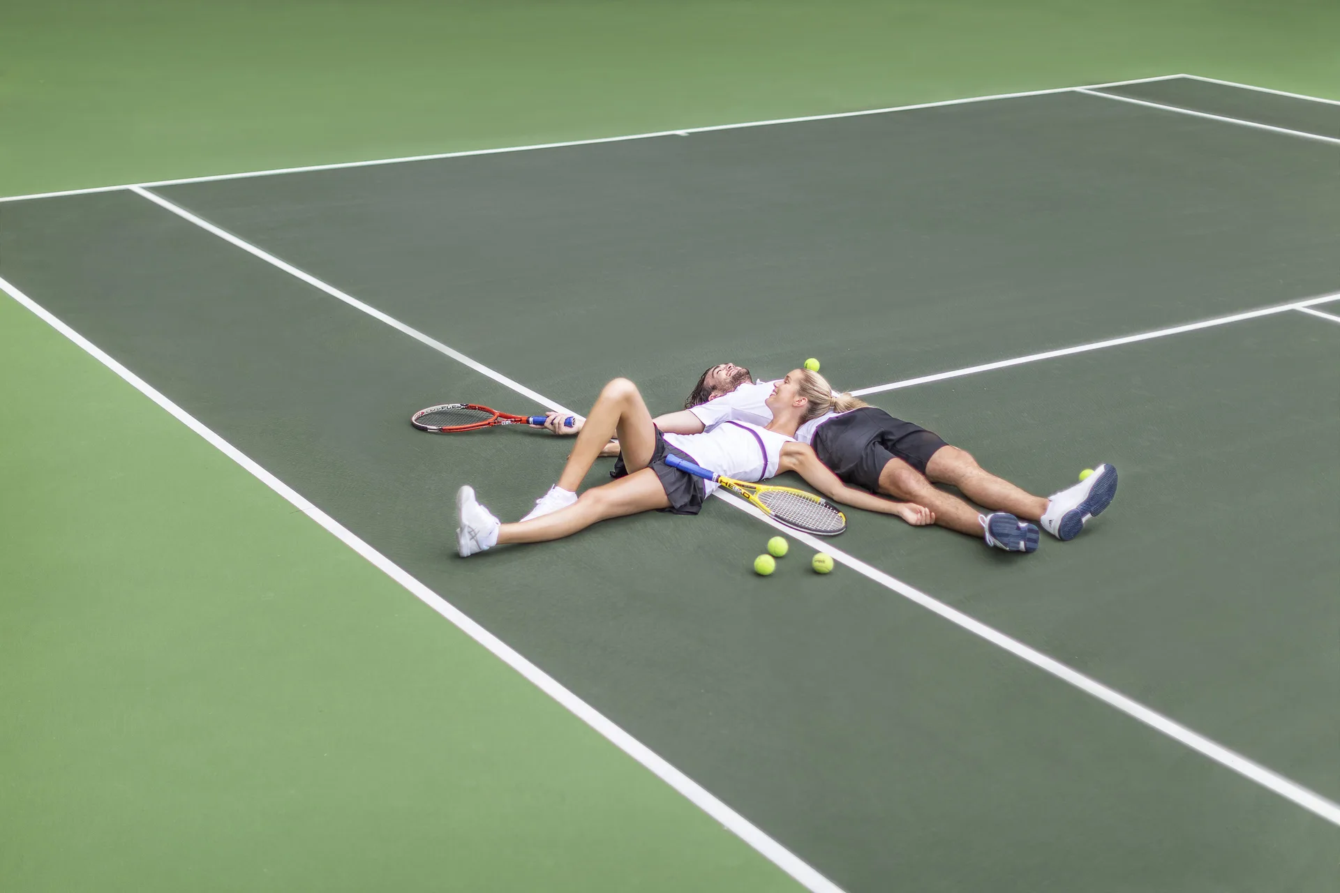 Two guests rest with tennis rackets and balls on a court at Couples Tower Isle.