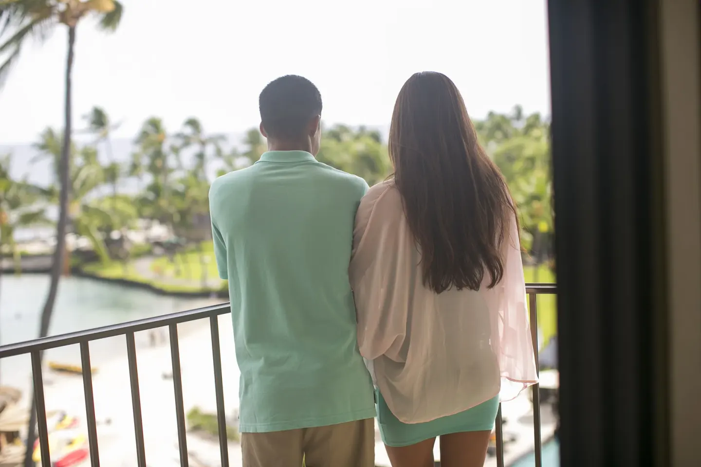 Couple on a balcony at Courtyard King Kamehameha's Kona Beach Hotel overlooking water and palms.