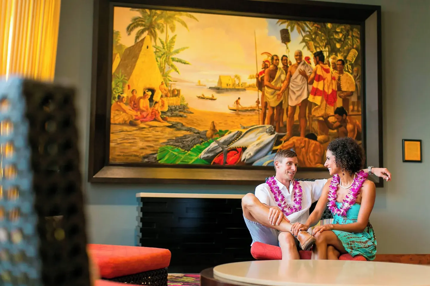 Guests seated beneath a large Hawaiian mural at Courtyard King Kamehameha's Kona Beach Hotel.