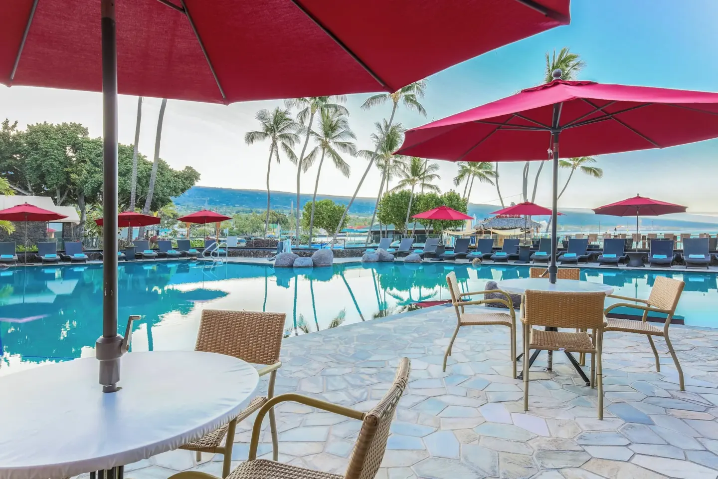Poolside tables and red umbrellas at Courtyard King Kamehameha's Kona Beach Hotel.