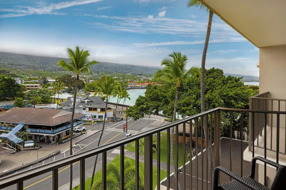Room balcony with chairs, town, palms, bay, and mountains at Courtyard King Kamehameha's Kona Beach Hotel.
