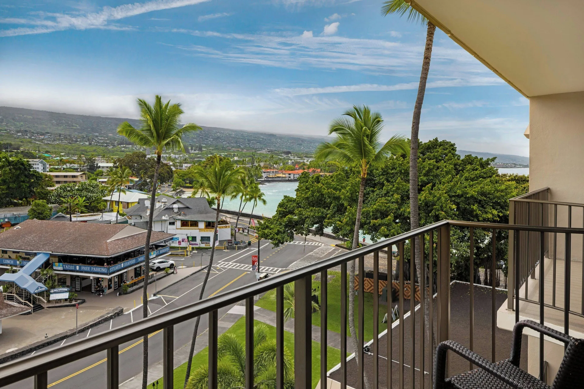 Room balcony with chairs, town, palms, bay, and mountains at Courtyard King Kamehameha's Kona Beach Hotel.