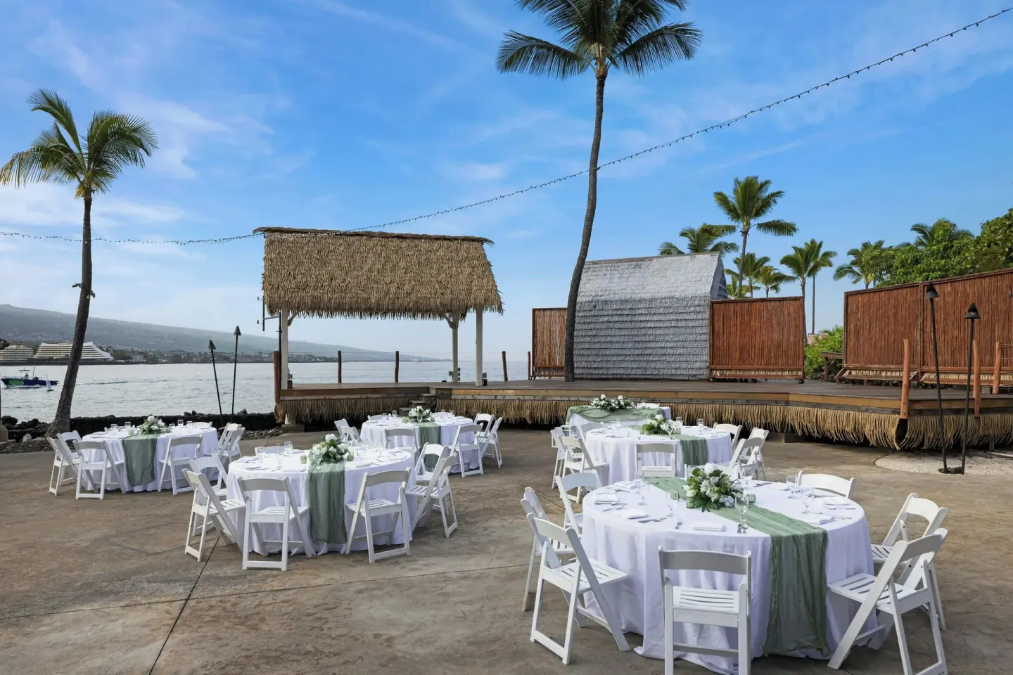 Round reception tables and a thatched stage by the bay at Courtyard King Kamehameha's Kona Beach Hotel.