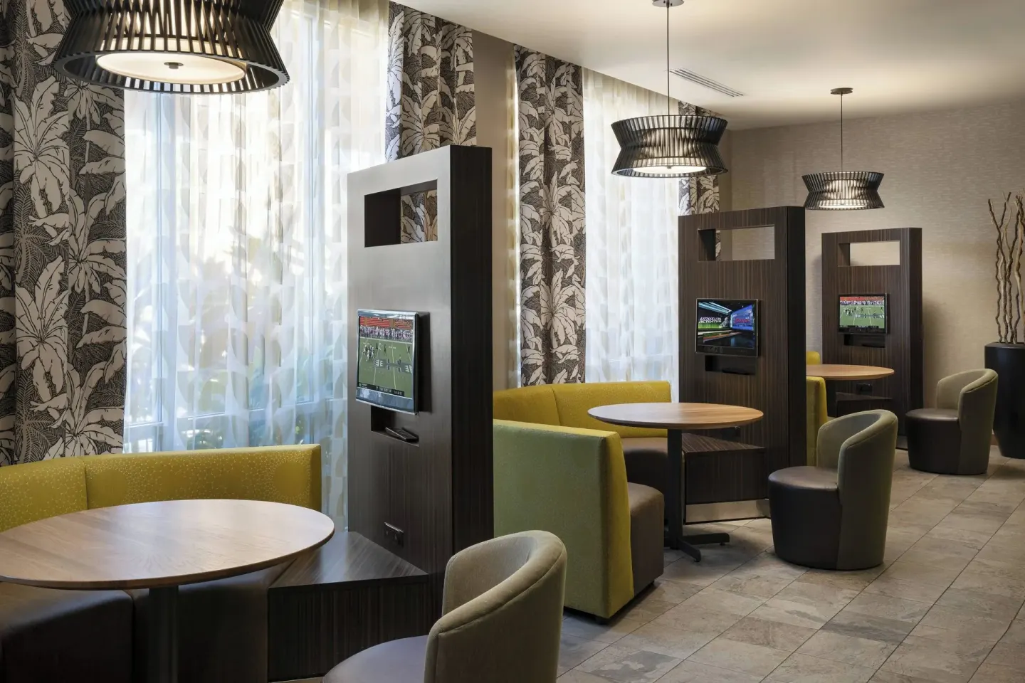 Lobby booths with round tables and mounted televisions at Courtyard Maui Kahului Airport.