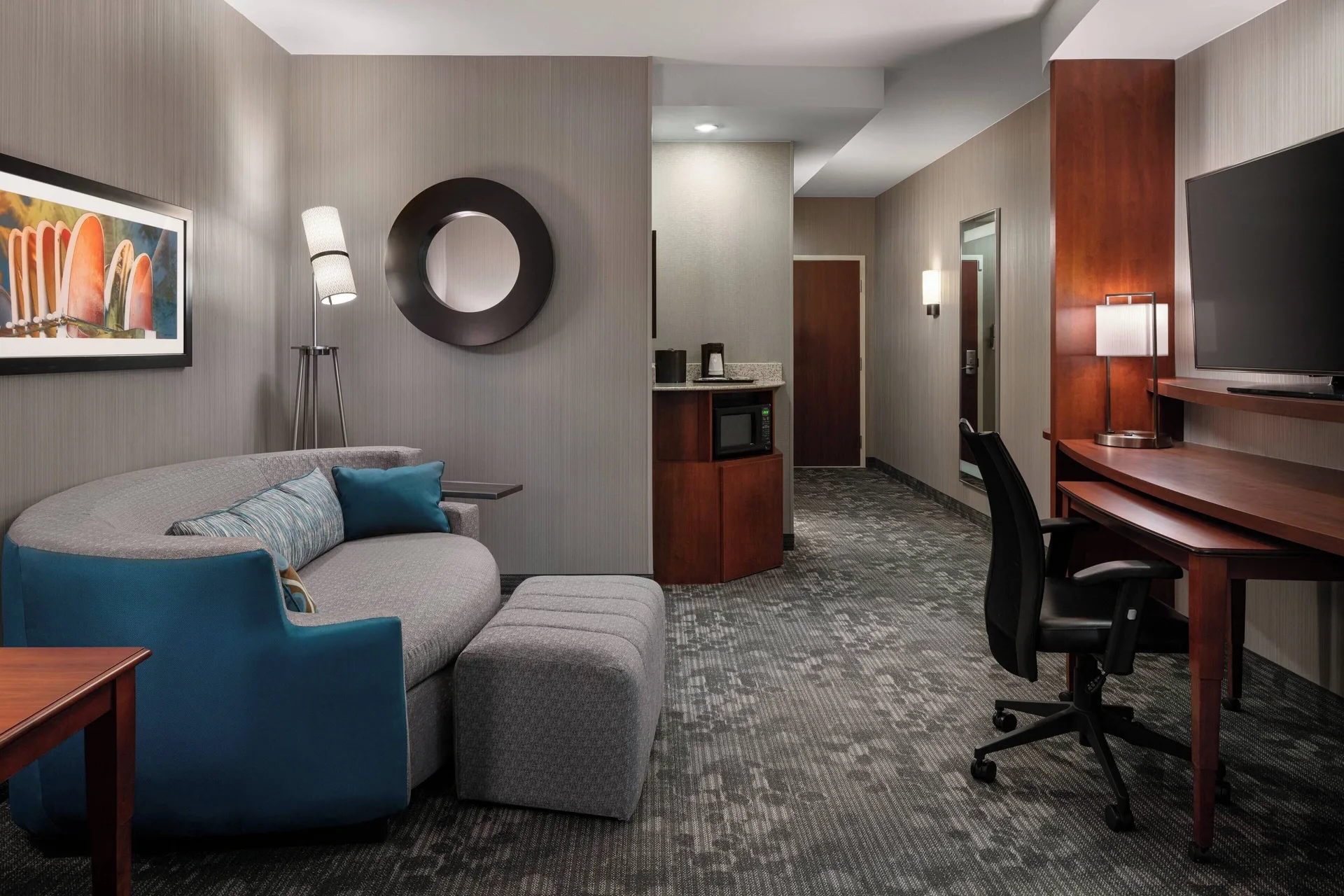 Junior room sitting area with sofa bed, ottoman, desk, TV, and entry at Courtyard Maui Kahului Airport.
