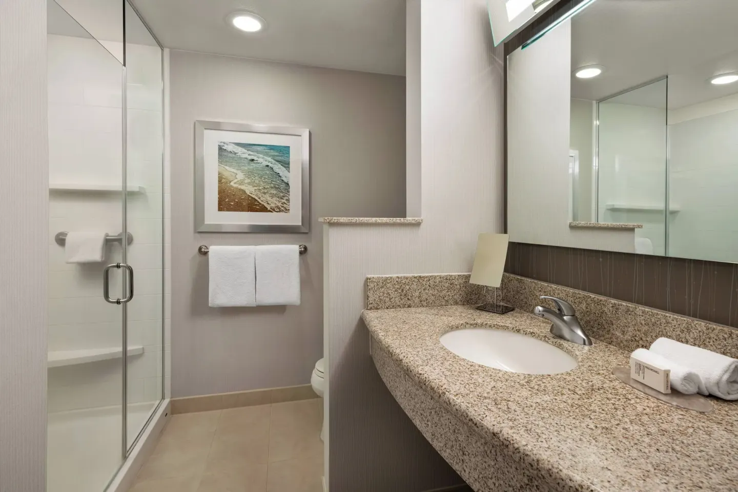 Guest bathroom with granite vanity and glass shower at Courtyard Maui Kahului Airport.