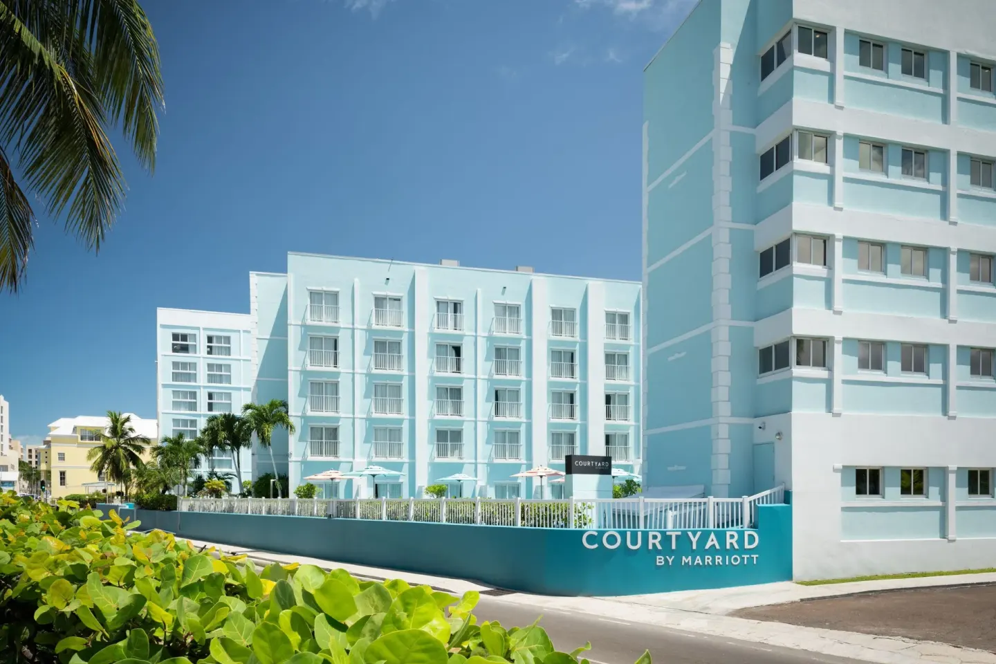 Exterior of Courtyard Nassau Downtown/Junkanoo Beach with blue buildings, balconies, palms, and street frontage.