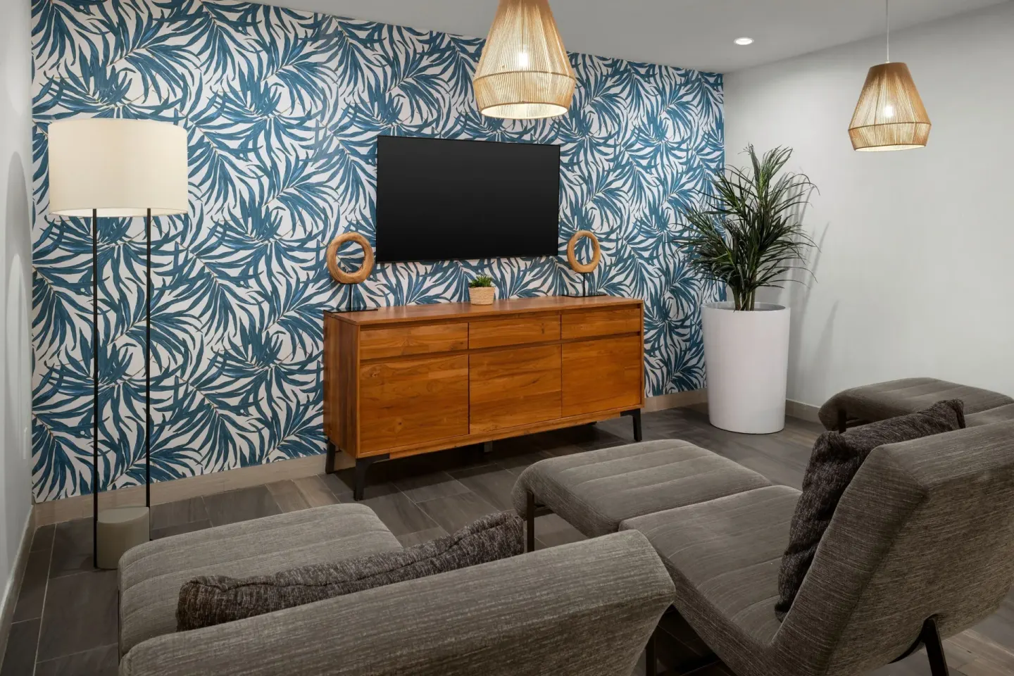 Media lounge at Courtyard Nassau Downtown/Junkanoo Beach with TV, gray chairs, and tropical wallpaper.