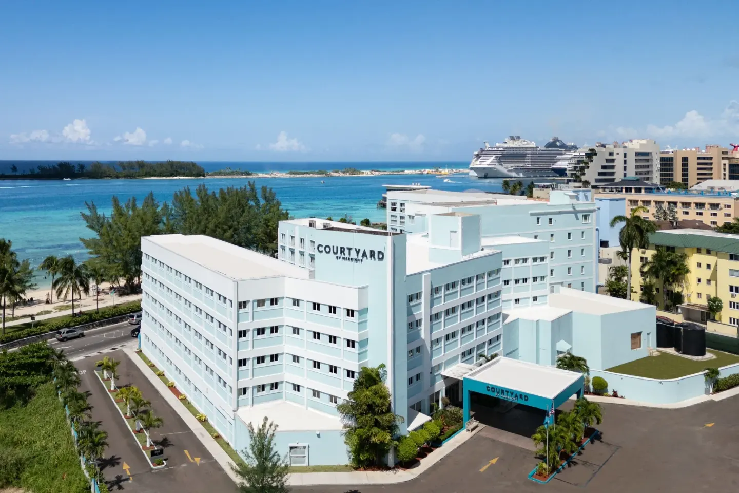 Aerial exterior of Courtyard Nassau Downtown/Junkanoo Beach beside turquoise water and nearby port.