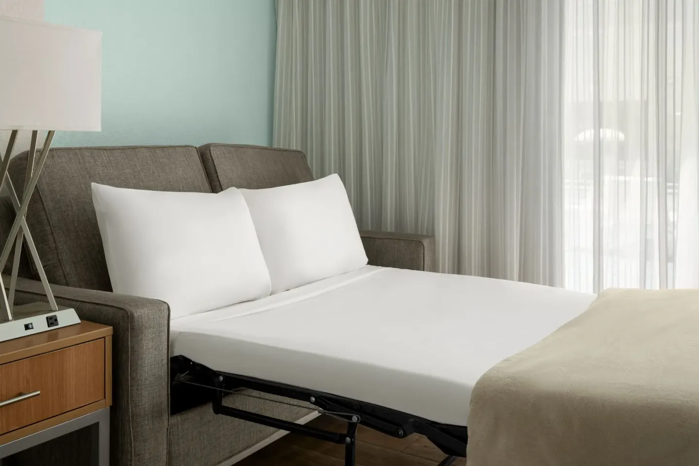 Pullout sofa bed by sheer curtains in a guest room at Courtyard Nassau Downtown/Junkanoo Beach.