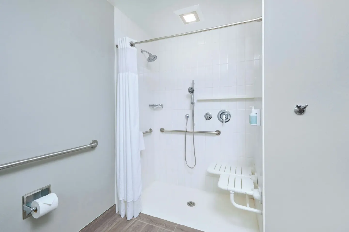Accessible roll-in shower with grab bars and folding seat at Courtyard Oahu North Shore.
