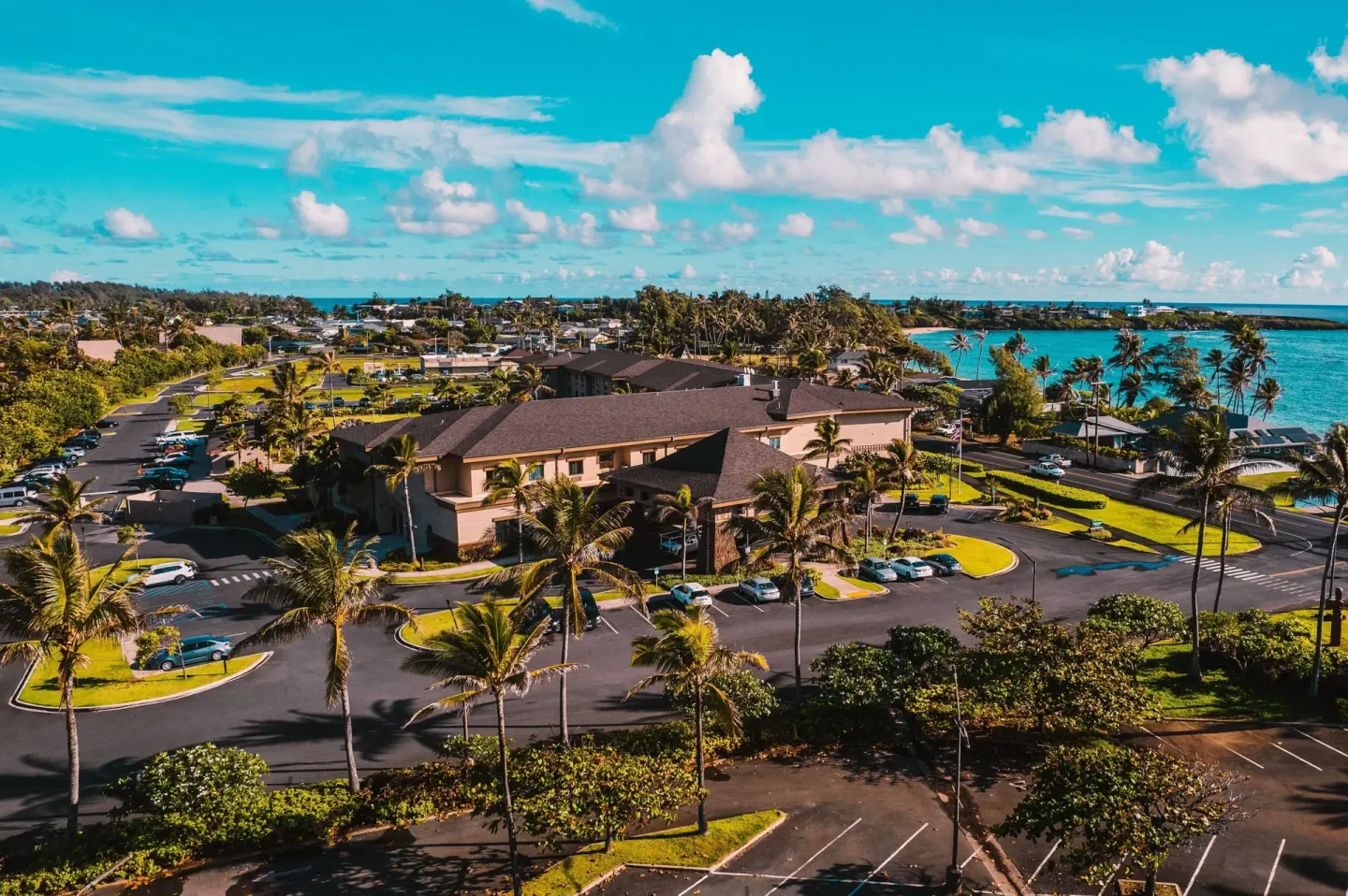 Aerial view of Courtyard Oahu North Shore near turquoise coastal water and palms.