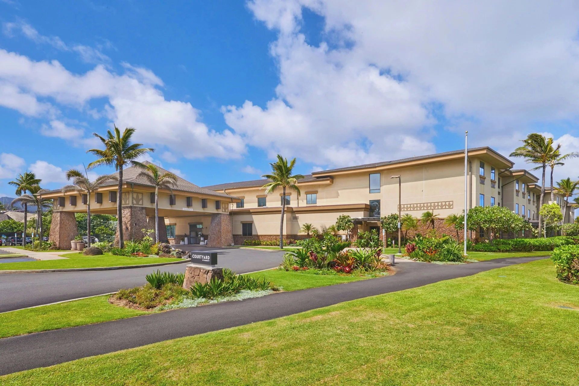 Daytime exterior with lawn, palms, and hotel sign at Courtyard Oahu North Shore.
