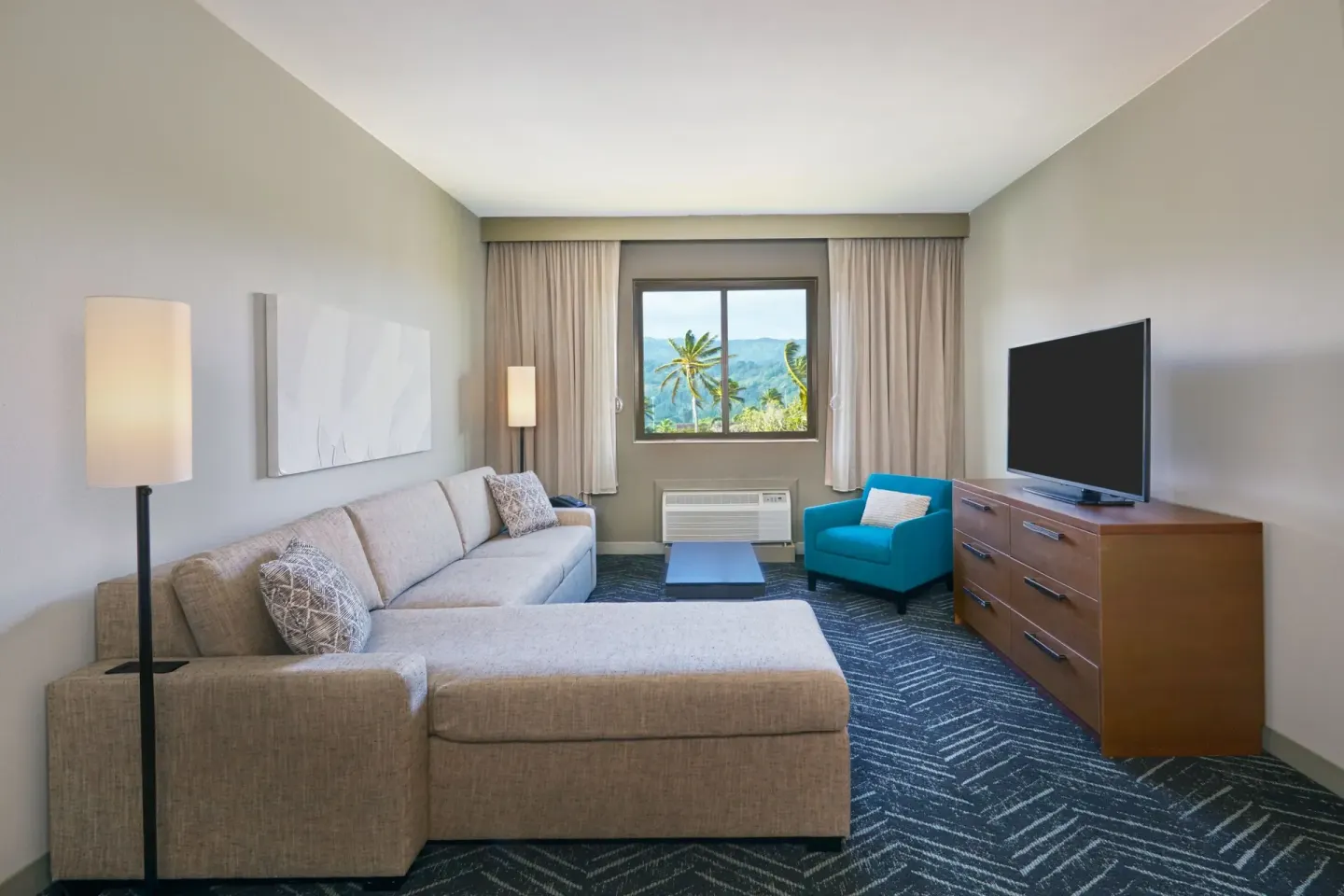 Guest room lounge with sectional sofa, TV, and palm view at Courtyard Oahu North Shore.