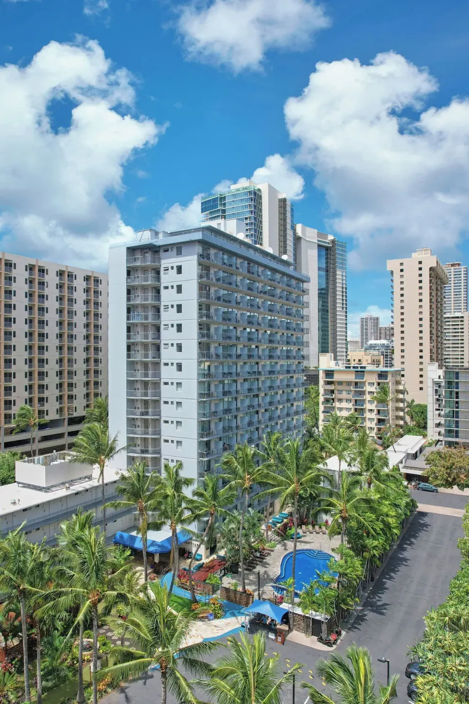 Courtyard Waikiki Beach rises above palms, pool areas and neighboring towers.
