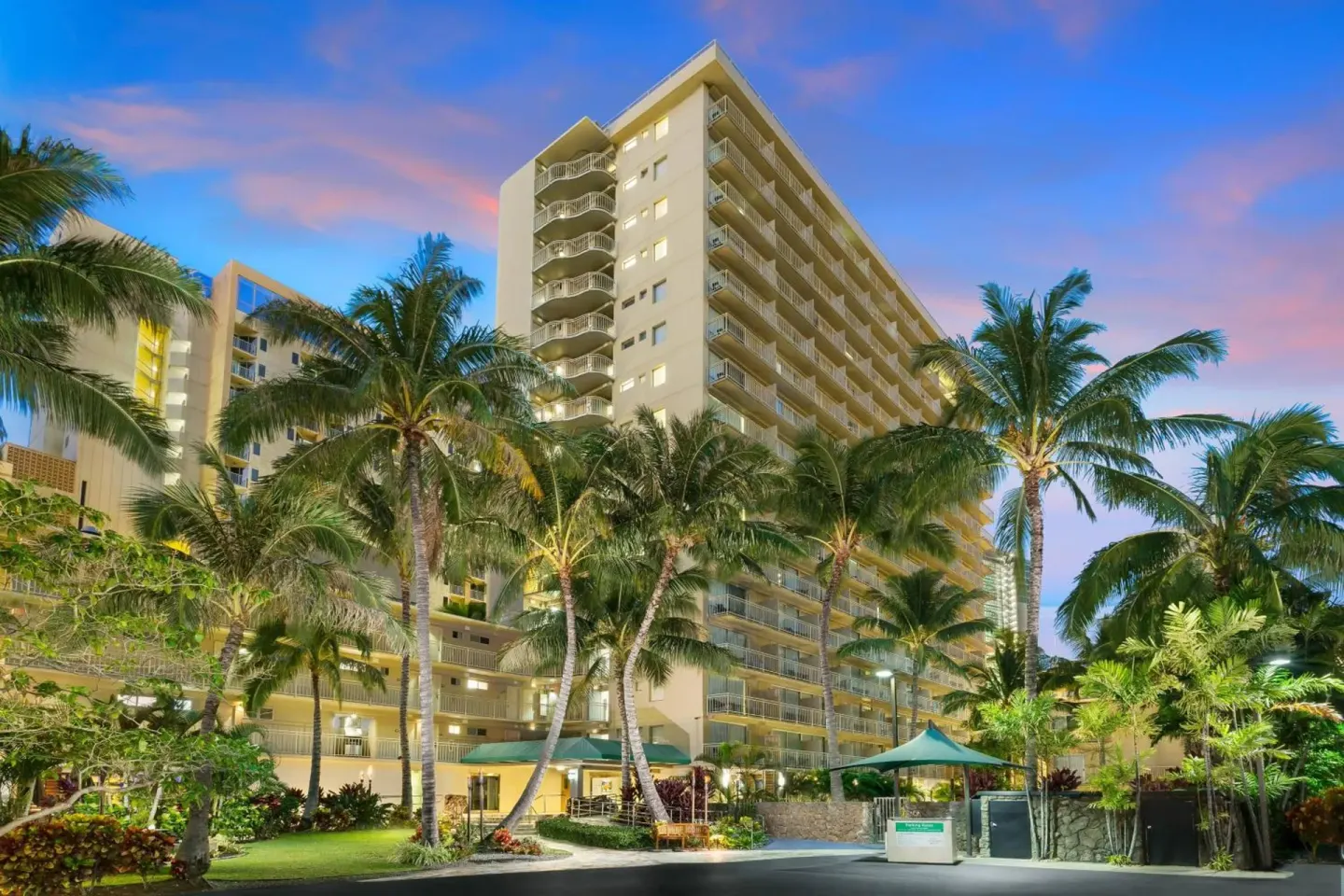 Exterior tower of Courtyard Waikiki Beach at dusk surrounded by palm trees.