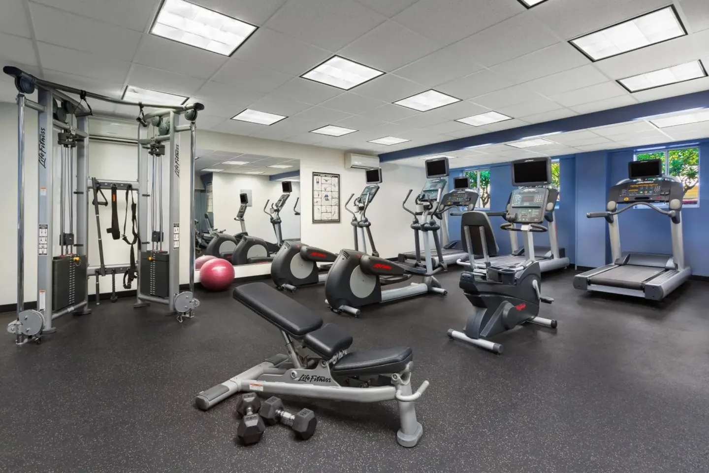 Fitness center with treadmills, ellipticals, weights, and cable machine at Courtyard Waikiki Beach.