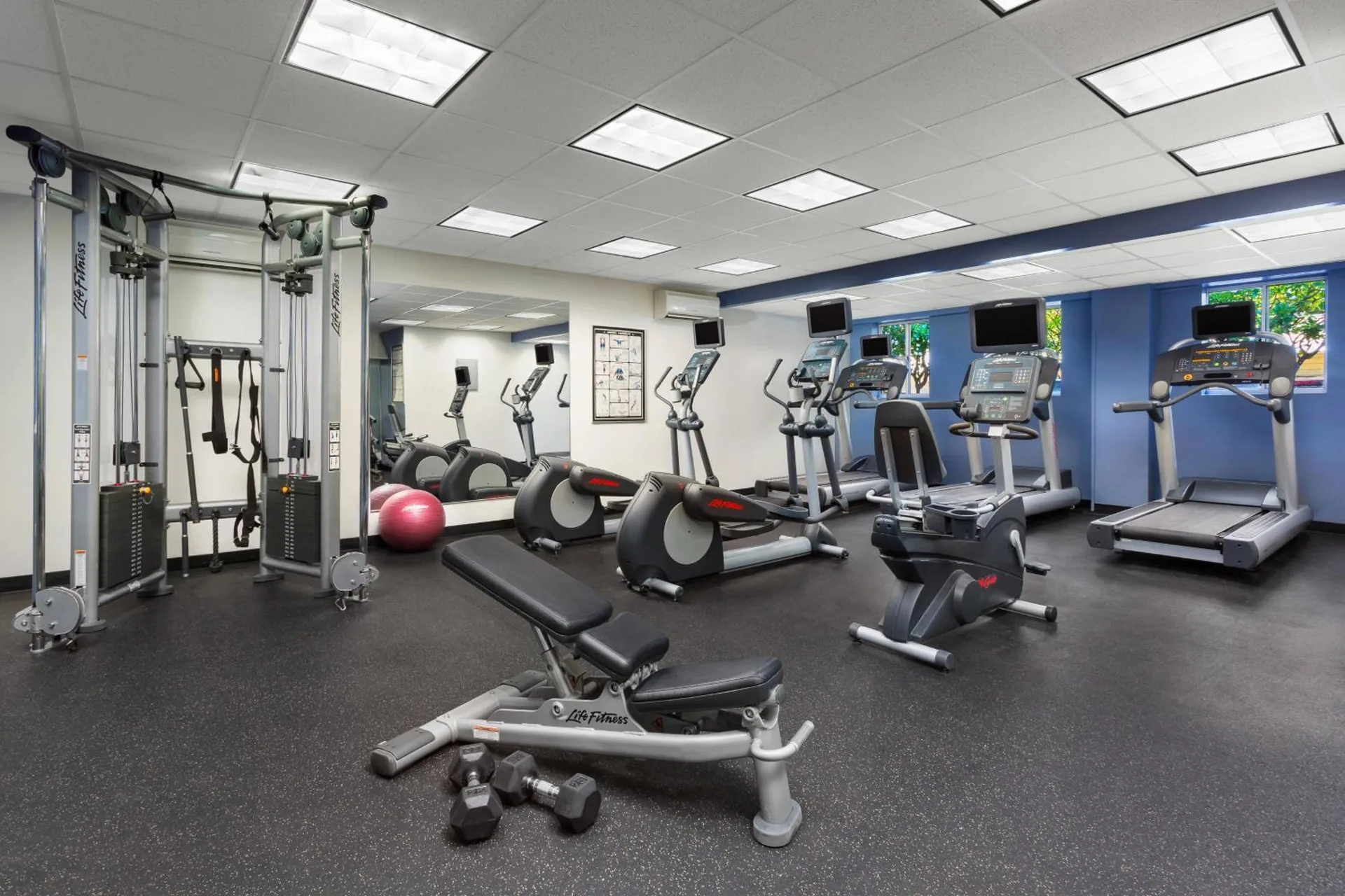 Fitness center with treadmills, ellipticals, weights, and cable machine at Courtyard Waikiki Beach.