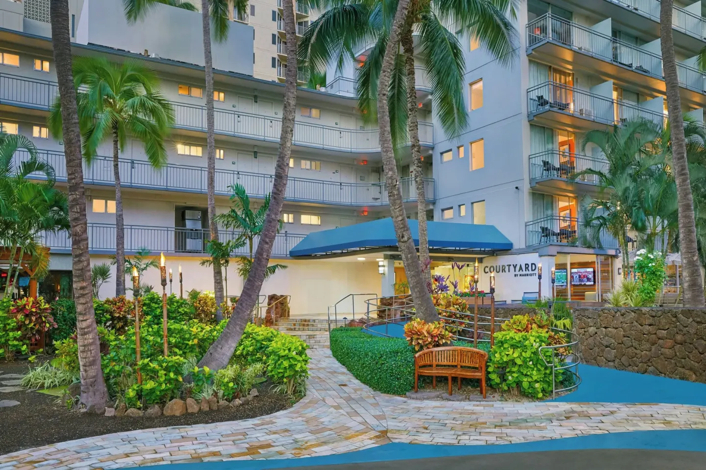 Garden courtyard entrance at Courtyard Waikiki Beach with palms, paths, and lit windows.