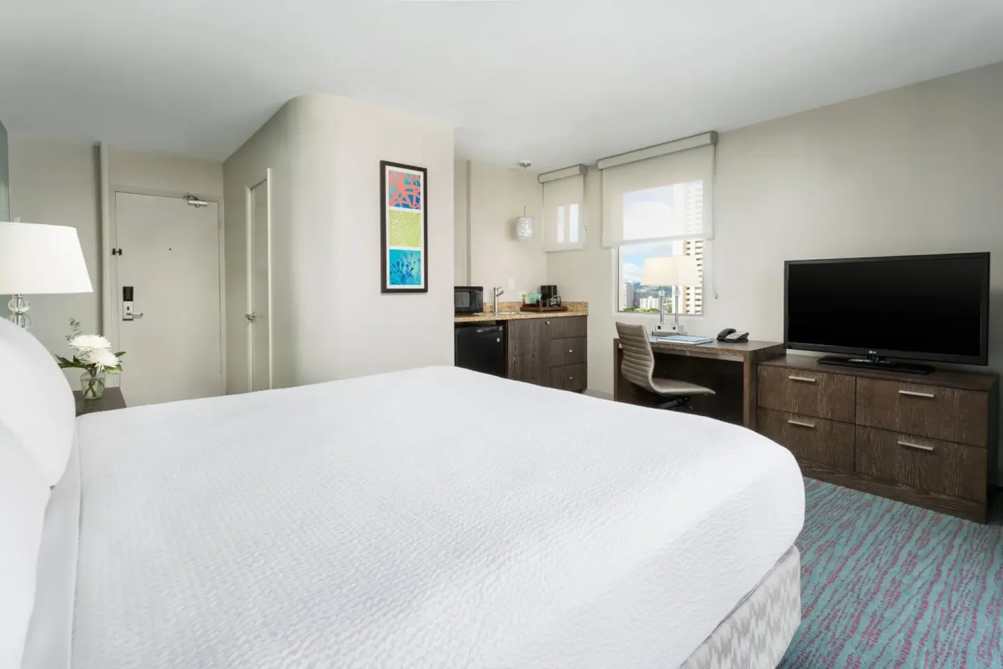 King guest room at Courtyard Waikiki Beach with desk, TV, and in-room refreshment area.