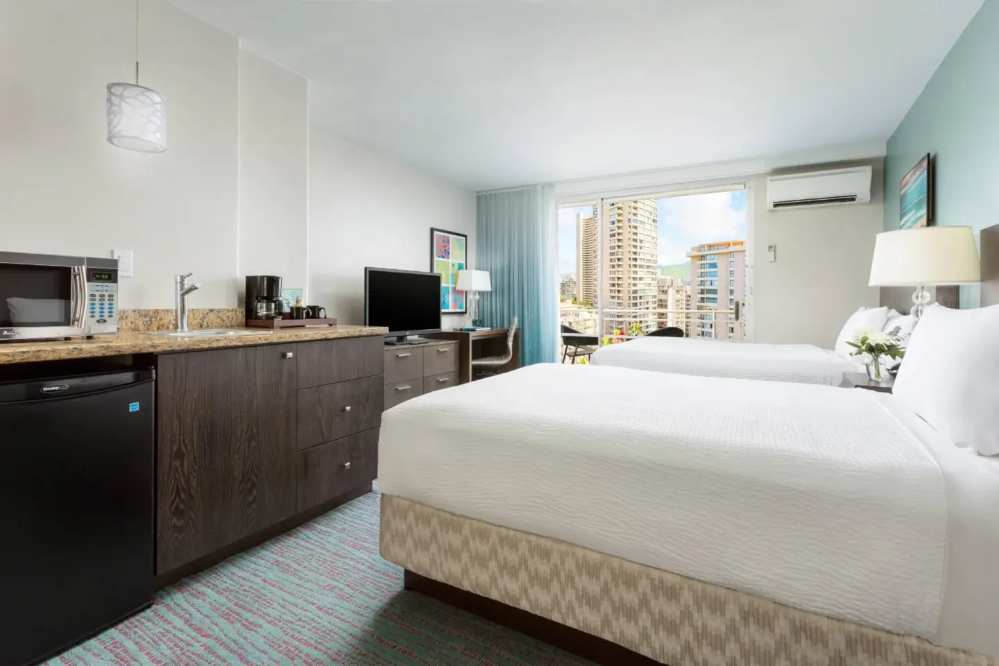 Guest room with two beds, kitchenette, TV, and balcony light at Courtyard Waikiki Beach.
