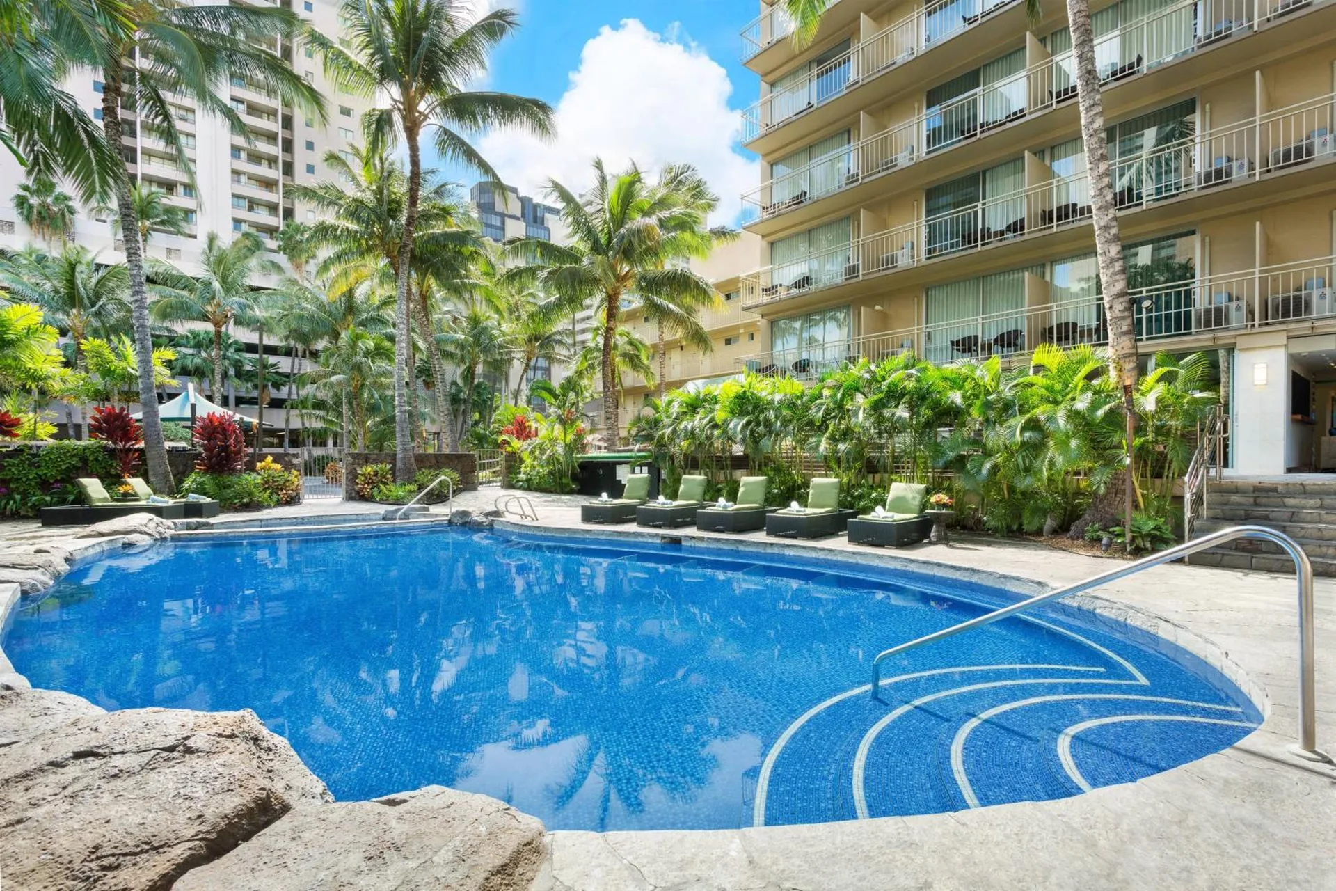 Outdoor pool with lounge chairs and palms at Courtyard Waikiki Beach.
