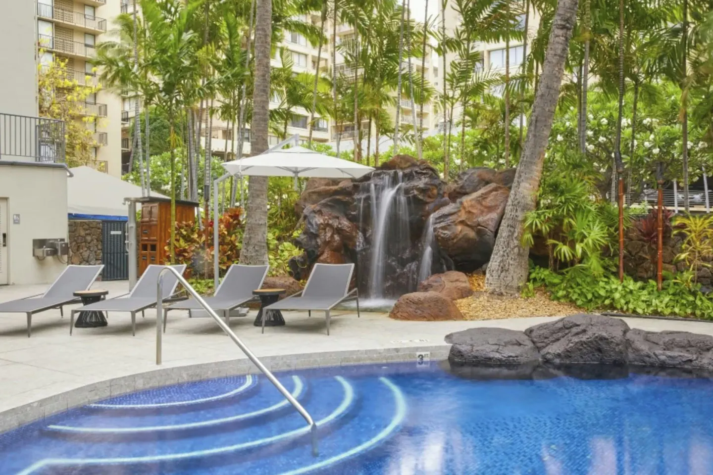 Pool steps, lounge chairs, and a rock waterfall at Courtyard Waikiki Beach.