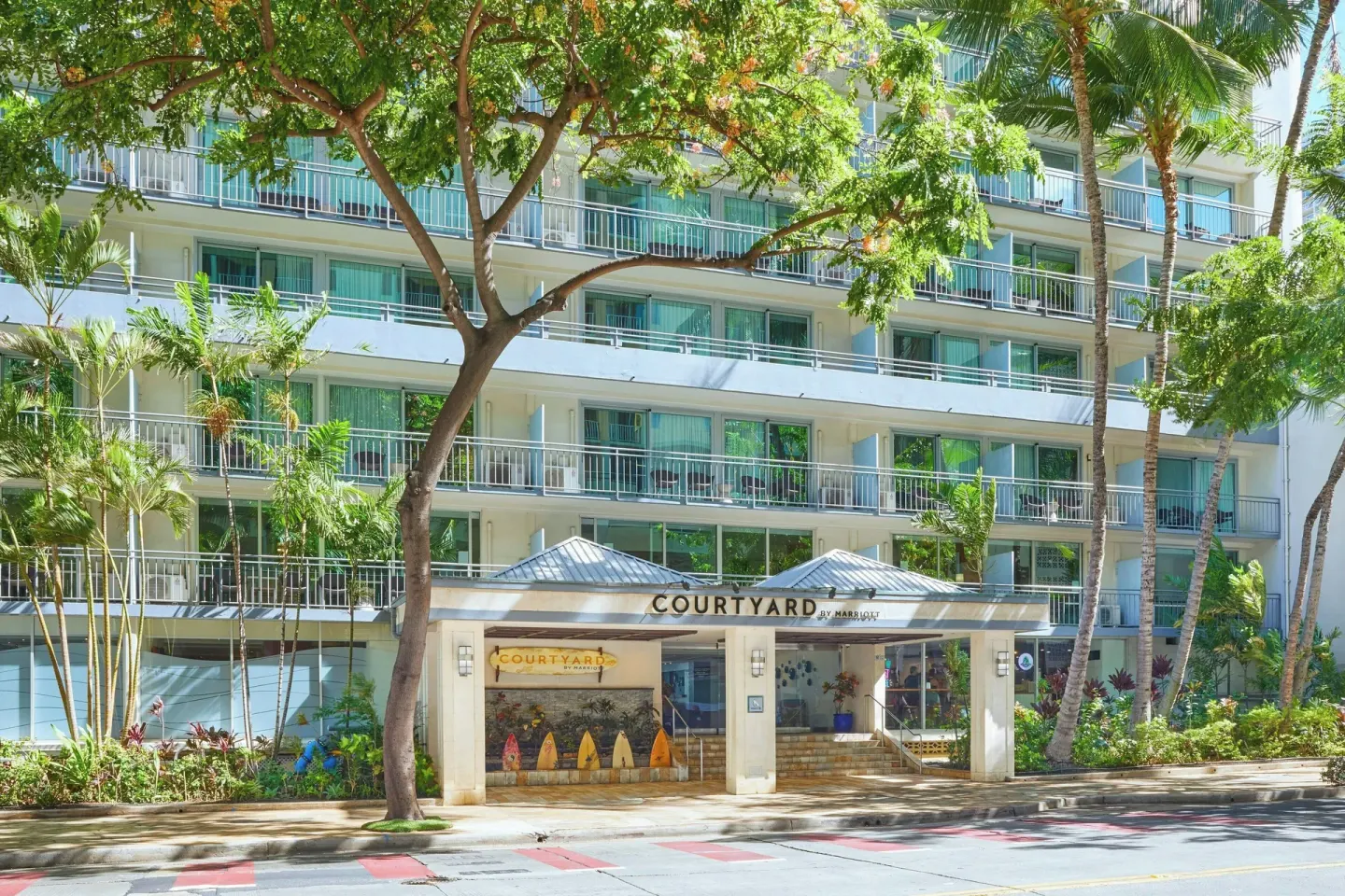 Street entrance of Courtyard Waikiki Beach with balconies, palms, and landscaping.