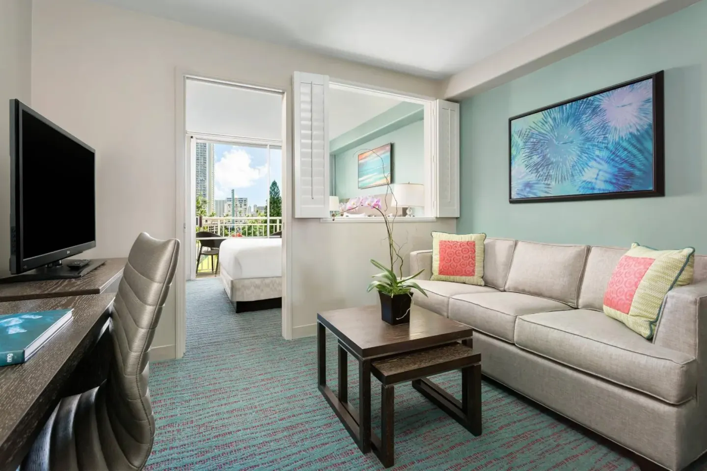 Suite sitting area with sofa, desk, TV, and bedroom doorway at Courtyard Waikiki Beach.