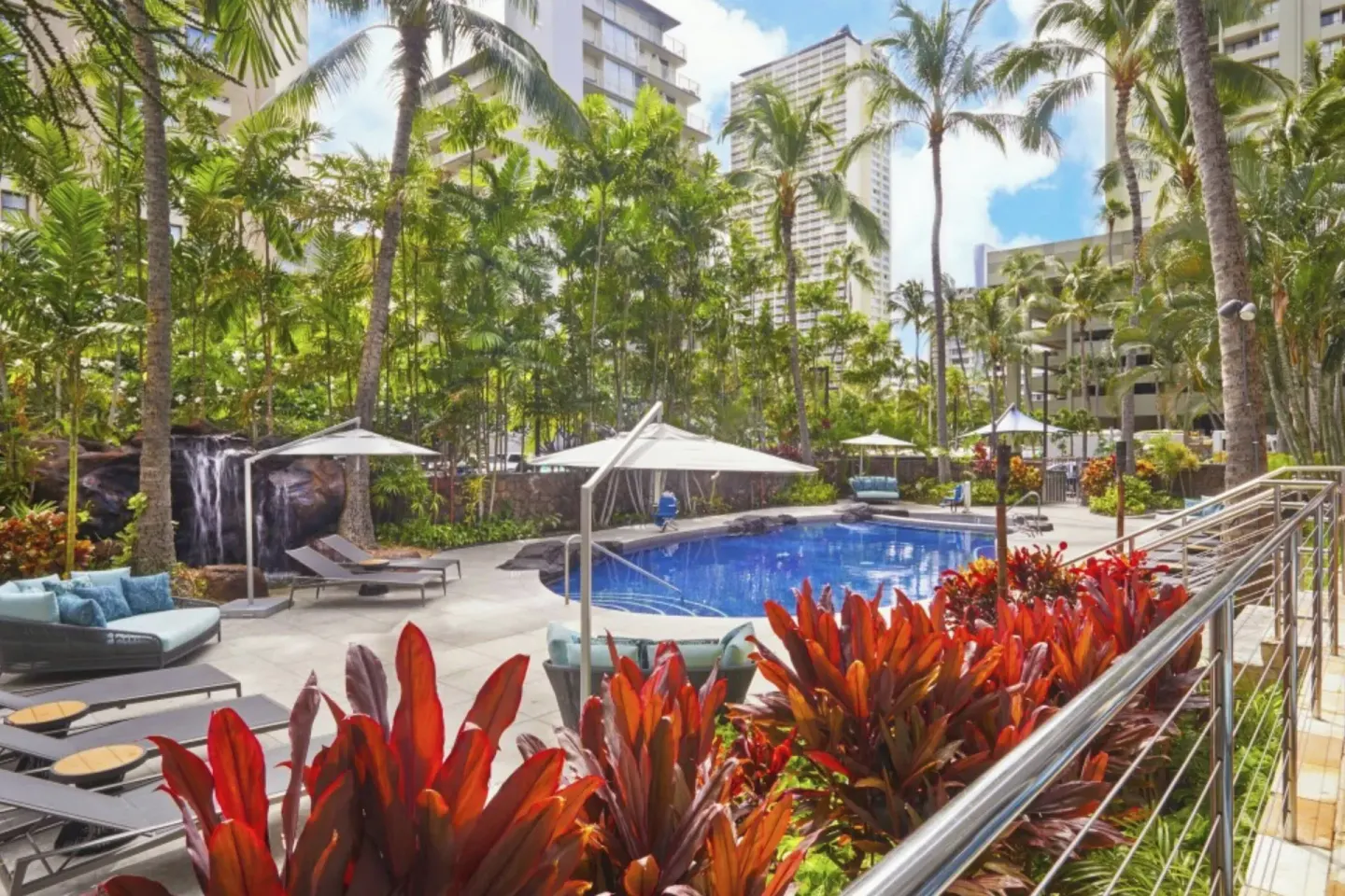 Tropical pool courtyard with palms, cabanas, and red foliage at Courtyard Waikiki Beach.