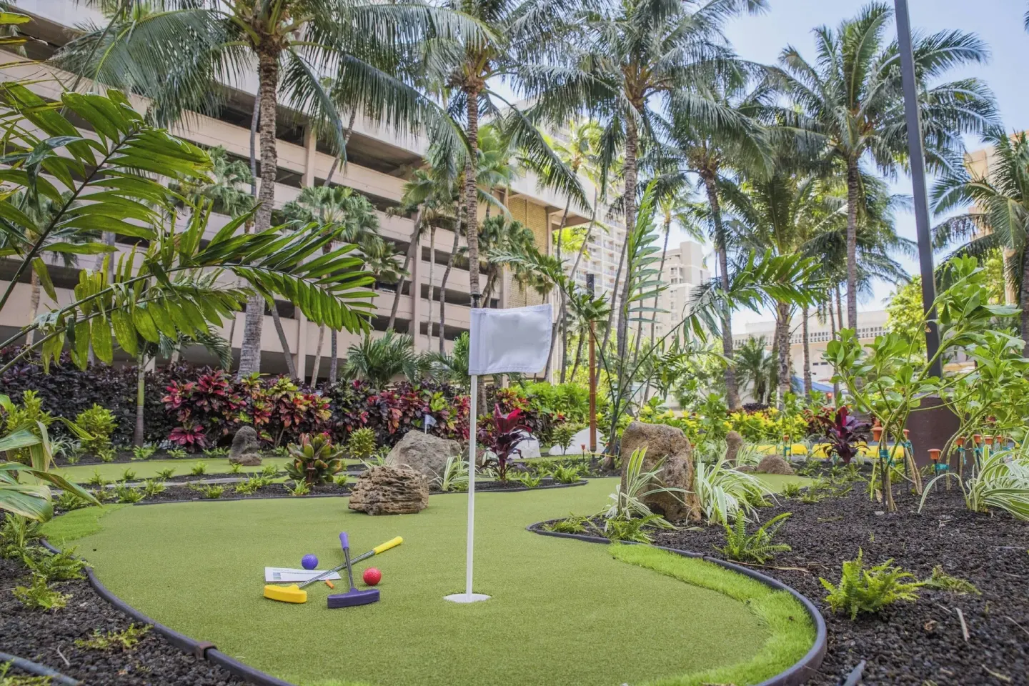 Tropical putting green with palms and golf clubs at Courtyard Waikiki Beach.