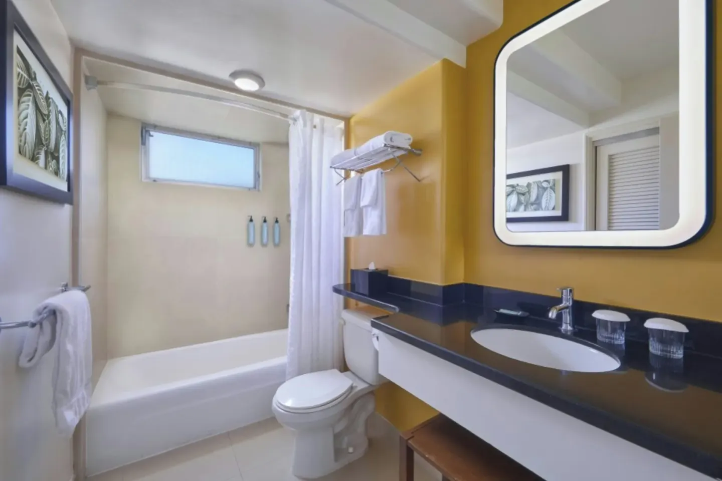 Deluxe balcony room bathroom with tub, shower curtain, vanity, and mirror at Courtyard Waikiki Beach.