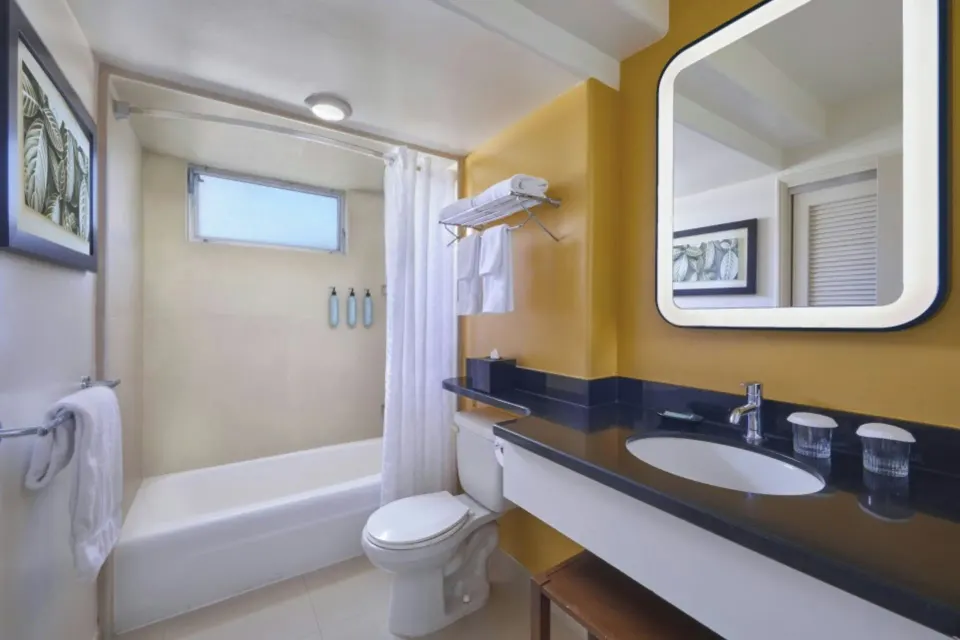 Deluxe balcony room bathroom with tub, shower curtain, vanity, and mirror at Courtyard Waikiki Beach.