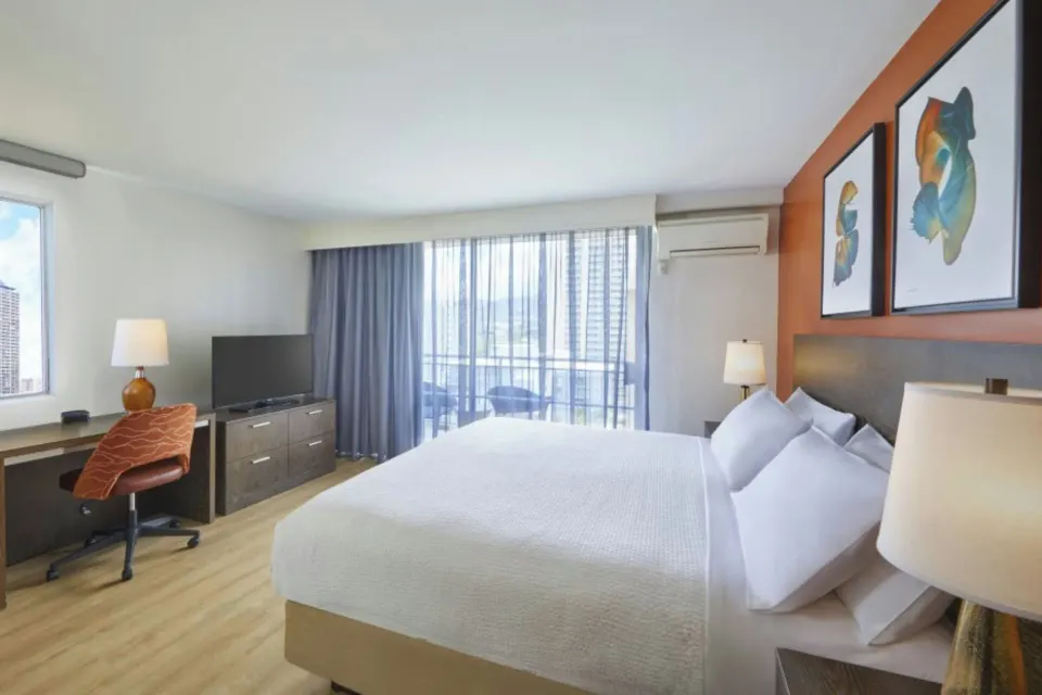Deluxe balcony room with king bed, desk, dresser, TV, and balcony doors at Courtyard Waikiki Beach.