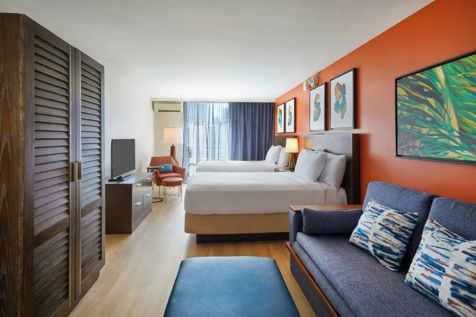 Junior Suite with two beds, sofa, closet doors, and balcony light at Courtyard Waikiki Beach.