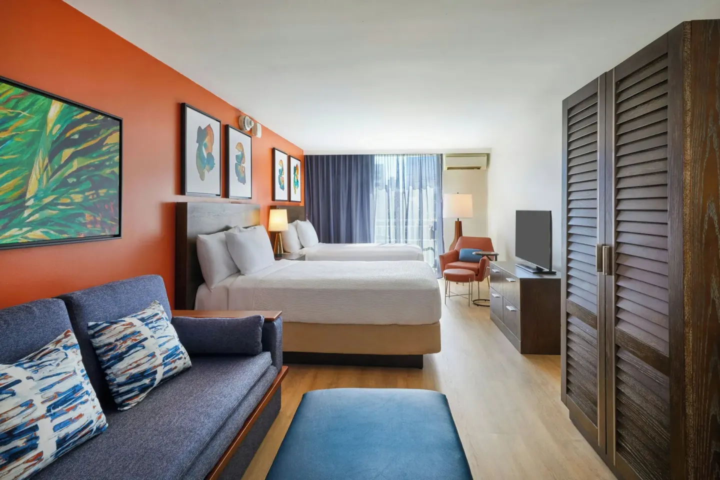 Junior Suite with two beds, sofa, TV, and balcony doors at Courtyard Waikiki Beach.