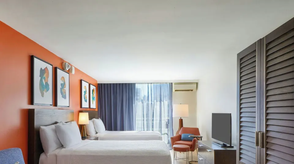 Junior Suite with two beds, TV, armchair, and balcony doors at Courtyard Waikiki Beach.
