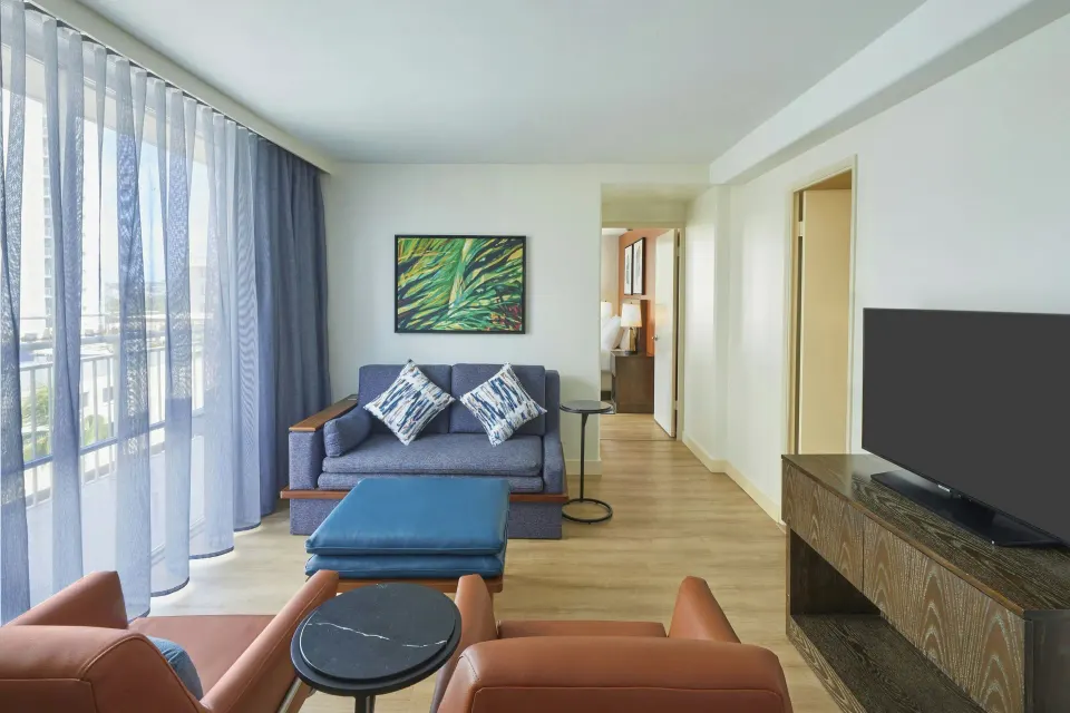 One-bedroom corner suite living area with sofa and TV at Courtyard Waikiki Beach.