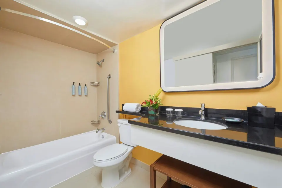 Suite bathroom with tub-shower, vanity, and lighted mirror at Courtyard Waikiki Beach.