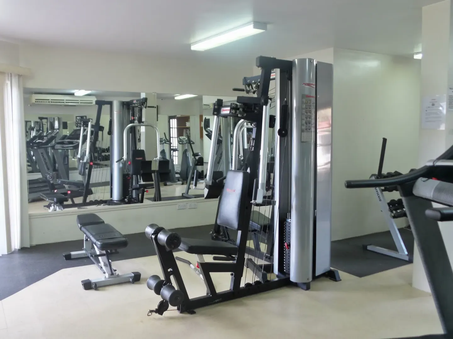 Fitness room with strength machine, bench, treadmill, and mirrors at Coyaba Beach Resort.