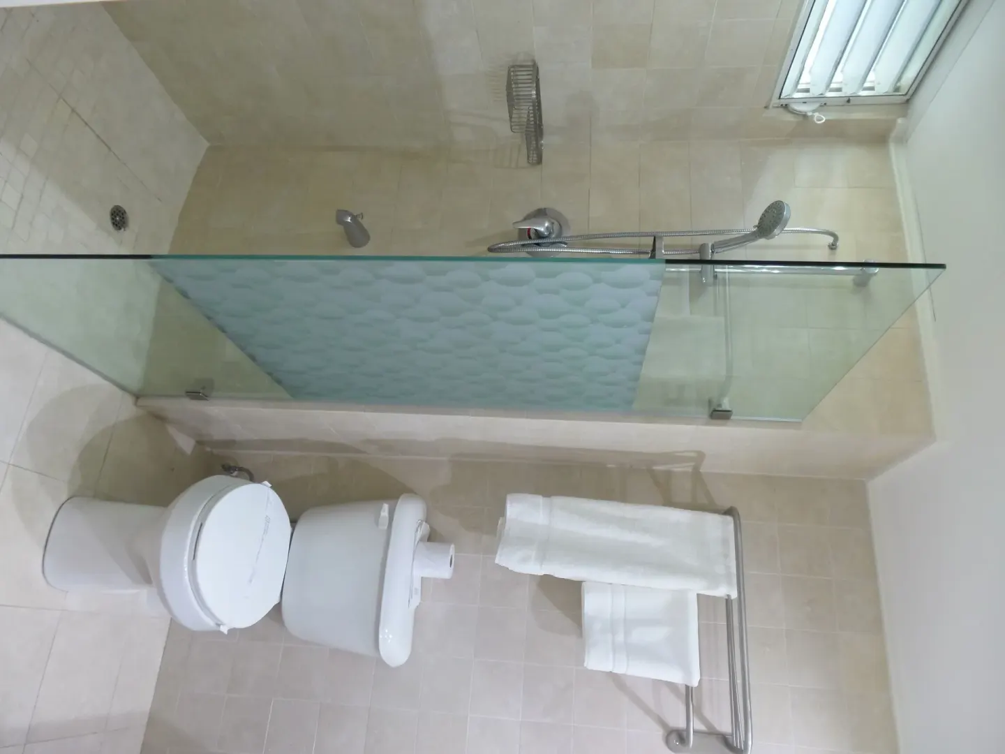 Guest bathroom with glass shower, toilet, and towel rack at Coyaba Beach Resort.